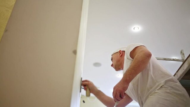 Plasterer in white cap evens plaster wall using the trowel.