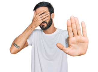 Young hispanic man wearing casual white t shirt covering eyes with hands and doing stop gesture with sad and fear expression. embarrassed and negative concept.