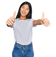 Beautiful young asian woman wearing casual white t shirt approving doing positive gesture with hand, thumbs up smiling and happy for success. winner gesture.