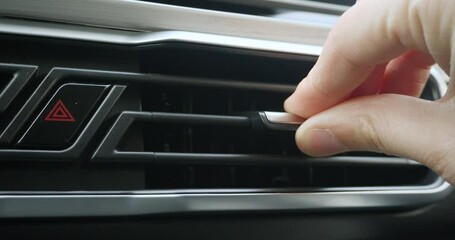 Close-up of a man's hand adjusting the ventilation grill on the console inside the car.