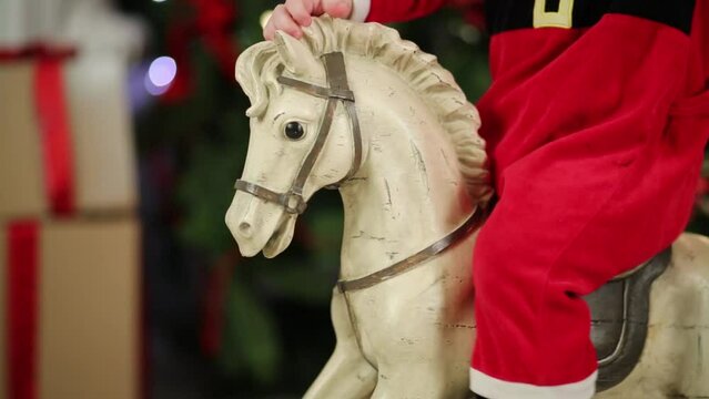Part of body of little kid in Santa costume on rocking horse 