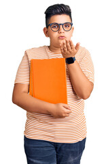 Little boy kid holding book wearing glasses looking at the camera blowing a kiss with hand on air being lovely and sexy. love expression.