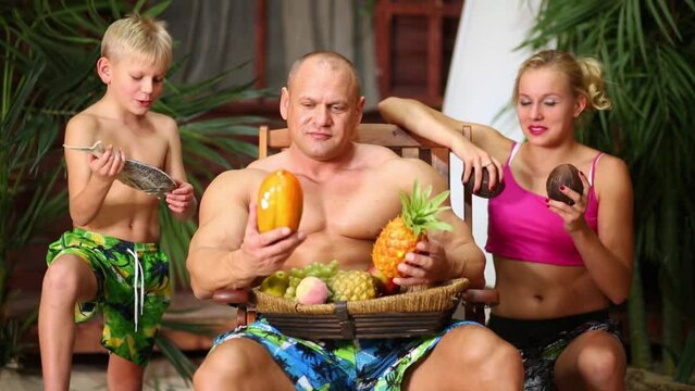 Family of three on beach near bungalow with basket full fruits.