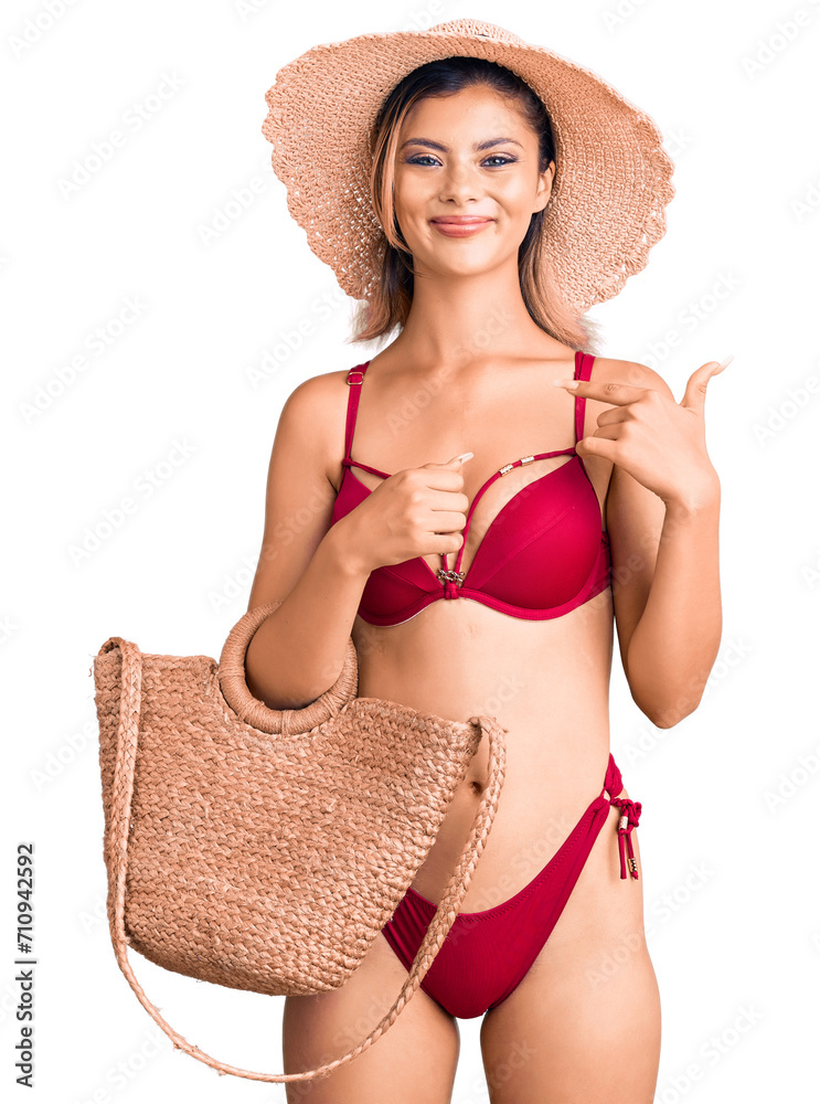 Sticker Young beautiful woman wearing bikini and hat holding summer wicker handbag pointing finger to one self smiling happy and proud