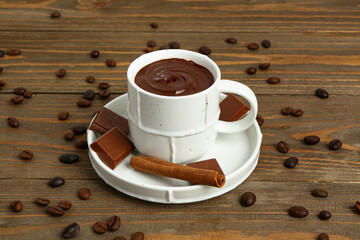 Cup of tasty melted chocolate, coffee beans and cinnamon on wooden background