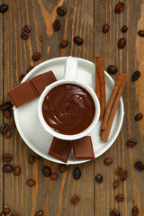 Cup of tasty melted chocolate, coffee beans and cinnamon on wooden background