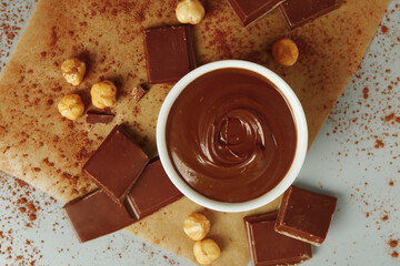 Composition with bowl of tasty melted chocolate and nuts on light background, closeup