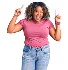 Young african american plus size woman wearing casual clothes smiling amazed and surprised and pointing up with fingers and raised arms.