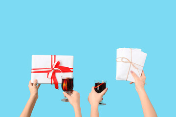 Female hands with glasses of warm mulled wine and gift boxes on blue background