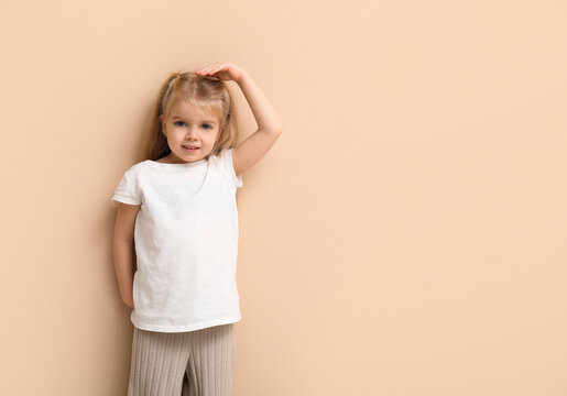 Cute little girl measuring height on beige background