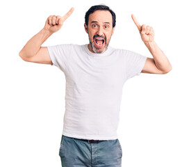Middle age handsome man wearing casual t-shirt smiling amazed and surprised and pointing up with fingers and raised arms.