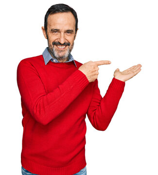 Middle age hispanic man wearing casual clothes amazed and smiling to the camera while presenting with hand and pointing with finger.