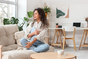 Young African-American woman with magazine sitting on sofa at home