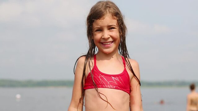 Cute smiling girl in a red swimsuit against the river.