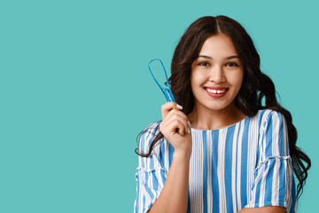 Happy young Asian woman with tongue scraper on blue background - obrazy, fototapety, plakaty