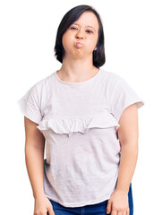 Brunette woman with down syndrome wearing casual white tshirt puffing cheeks with funny face. mouth inflated with air, crazy expression. - obrazy, fototapety, plakaty