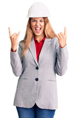 Beautiful young woman wearing architect hardhat shouting with crazy expression doing rock symbol with hands up. music star. heavy concept.