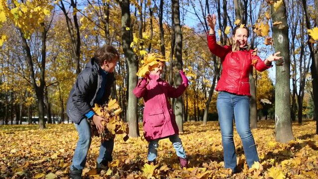 Mother and two children throw yellow fallen leaves in autumn park