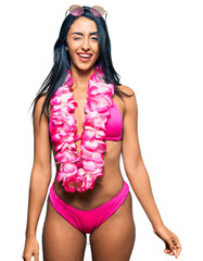 Beautiful hispanic woman wearing bikini and hawaiian lei winking looking at the camera with sexy...