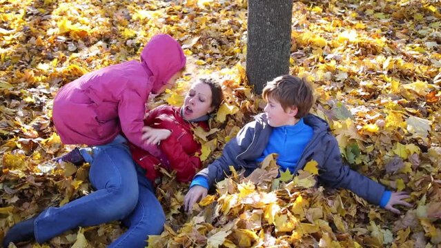 Mother and two children lie on many yellow fallen leaves