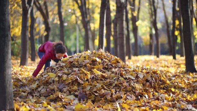 Mother and two children make big heap of yellow fallen leaves