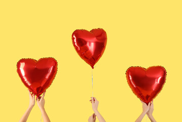 Female hands holding heart-shaped balloons on yellow background. Valentine's Day celebration
