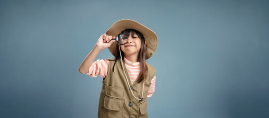 A little girl is wearing a camping clothes, holding a magnifying glass for studying.