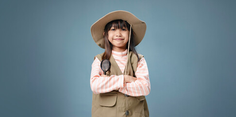 A little girl is wearing a camping clothes, holding a magnifying glass for studying.