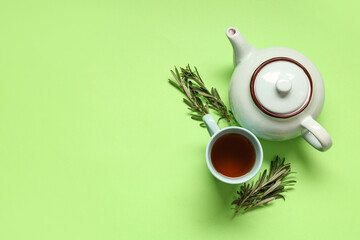 Teapot and cup of hot rosemary tea on green background
