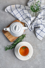 Cup and teapot of hot rosemary tea on grey background