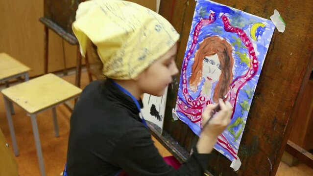 Close-up view of girl painting colorful picture at art class.