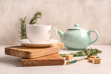 Wooden board with cup and teapot of hot rosemary tea on white background