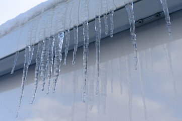 Icicles hanging from a roof gutter against a clear sky with snow on the edge and reflection on...