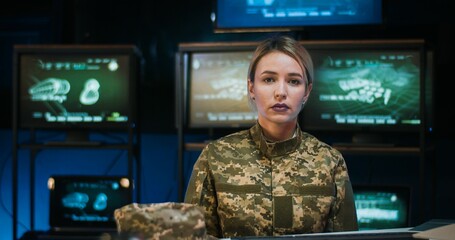 Portrait of pretty Caucasian female soldier sitting at desk in monitoring room, taking on cap and...