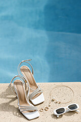 Elegant wedding shoes, gold accessories, and white glasses by poolside