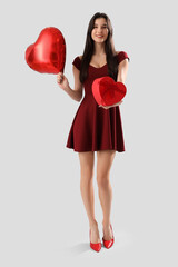 Beautiful young woman with heart-shaped air balloon and gift for Valentine's day on grey background