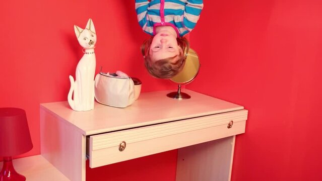 Little girl upside down in bedroom above dressing table