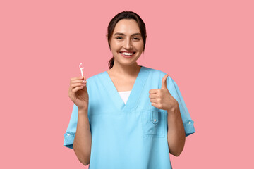 Young female dentist with floss toothpick showing thumb-up on pink background - obrazy, fototapety, plakaty
