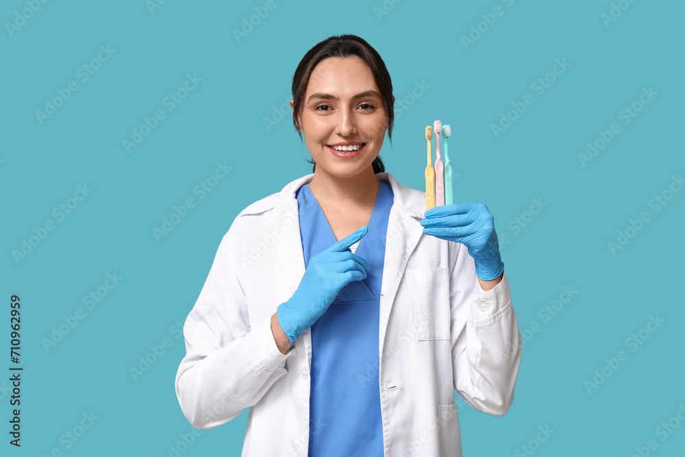 Wall mural young female dentist pointing at toothbrushes on blue background