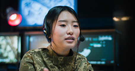Close up of Asian young woman in camouflage clothes and headset sitting at computer screen in...