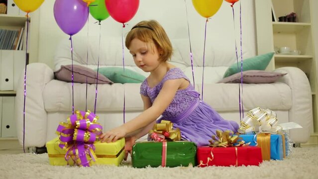 Little girl is sitting on the floor and examing gift-boxes.