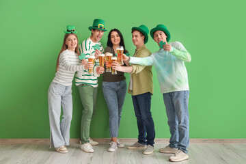 Group of young people with beer and paper clovers near green wall. St. Patrick's Day celebration