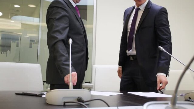 Two businessmen get up from table in meeting room and shake hands