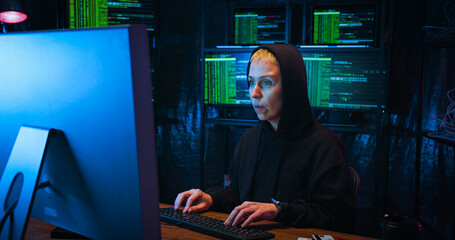 Caucasian woman coming in dark monitoring room and sitting in front of big screen of computer while working at night in cyberpolice. Female IT worker programming and creating program.