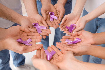 People with lavender awareness ribbons on light background, closeup. World Cancer Day