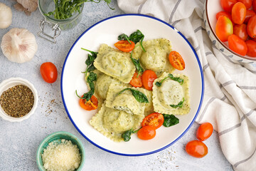 Bowl of tasty ravioli with vegetables on grey background