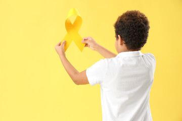 Little African-American boy with yellow ribbon on color background. Childhood cancer awareness concept