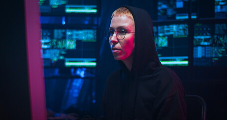 Caucasian cyberpolice woman in glasses and black hood sitting at computer screen as working at...