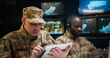 African American young man in headset typing on laptop computer and Caucasian soldier tapping on...