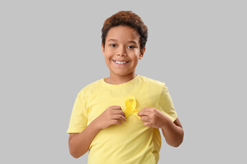 Cute little African-American boy with yellow ribbon on grey background. Childhood cancer awareness concept